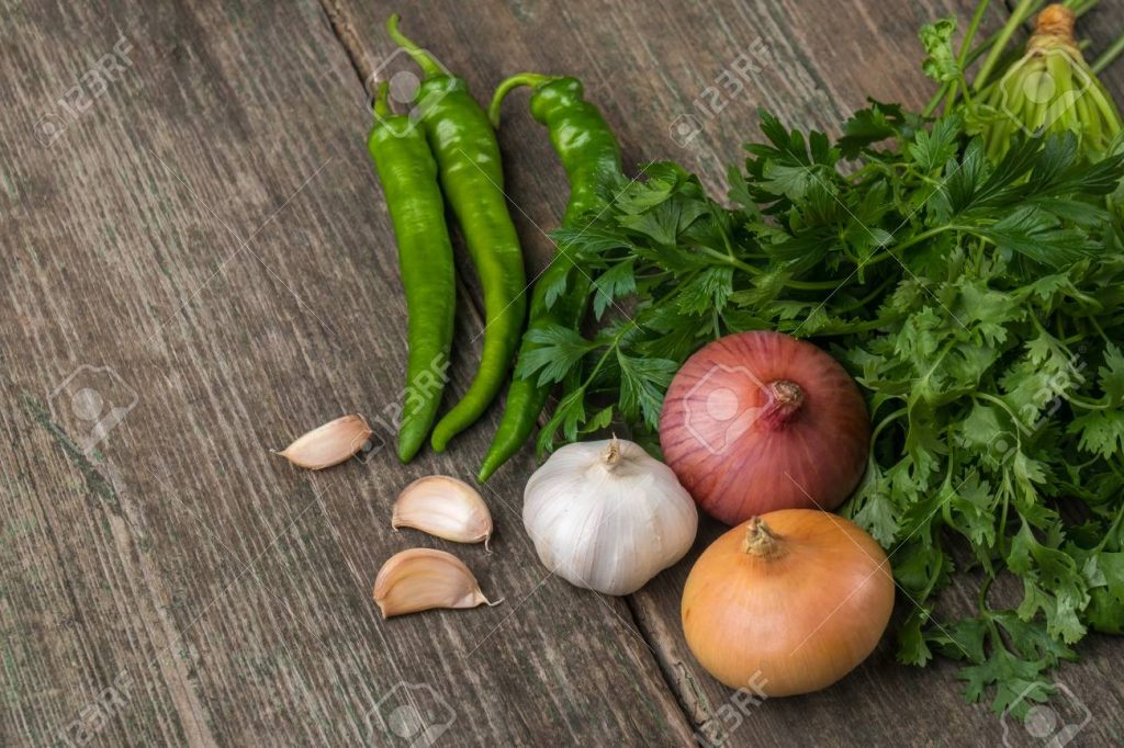 Onion, corn, garlic, pepper, coriander and parsley on an old wooden board.