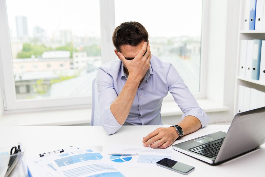 business, people, fail, paperwork and technology concept - businessman with laptop computer and papers working in office